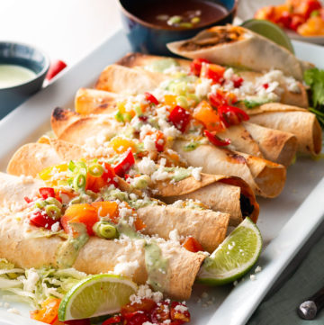 A platter of Birria Taquitos with toppings.